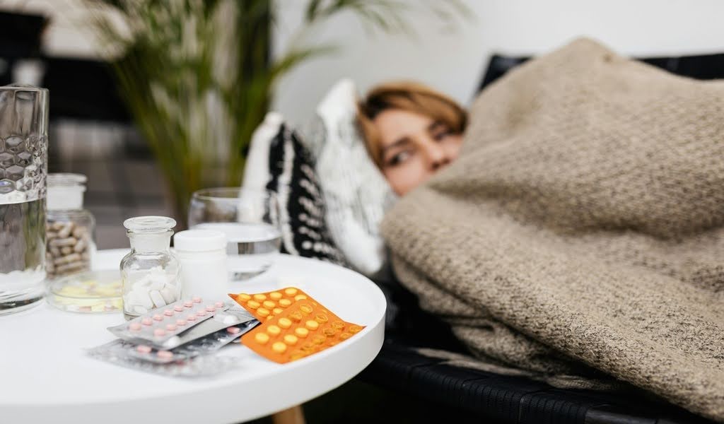 Blurred sick woman resting on sofa with pill strips on table in focus
