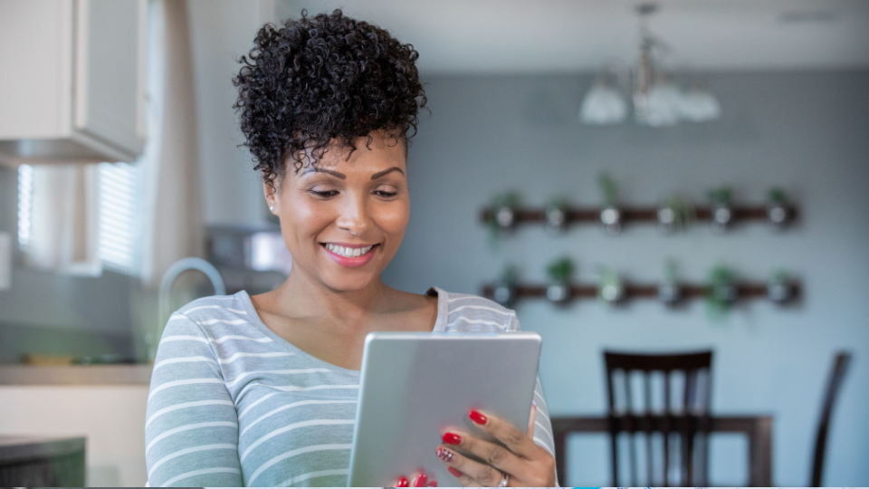 Woman smiling while holding and looking at a tablet.
