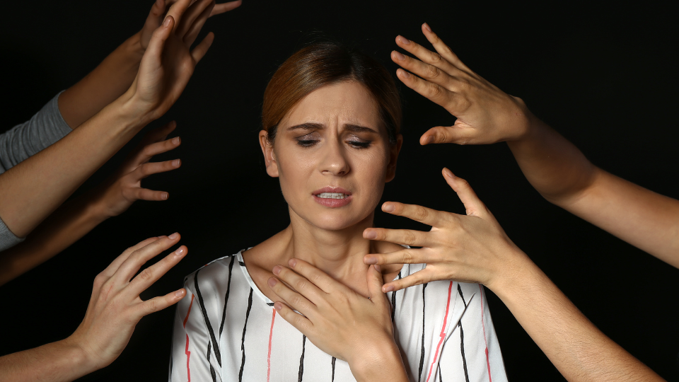 Women holding chest with multiple hands from others around her giving anxiety reaction.
