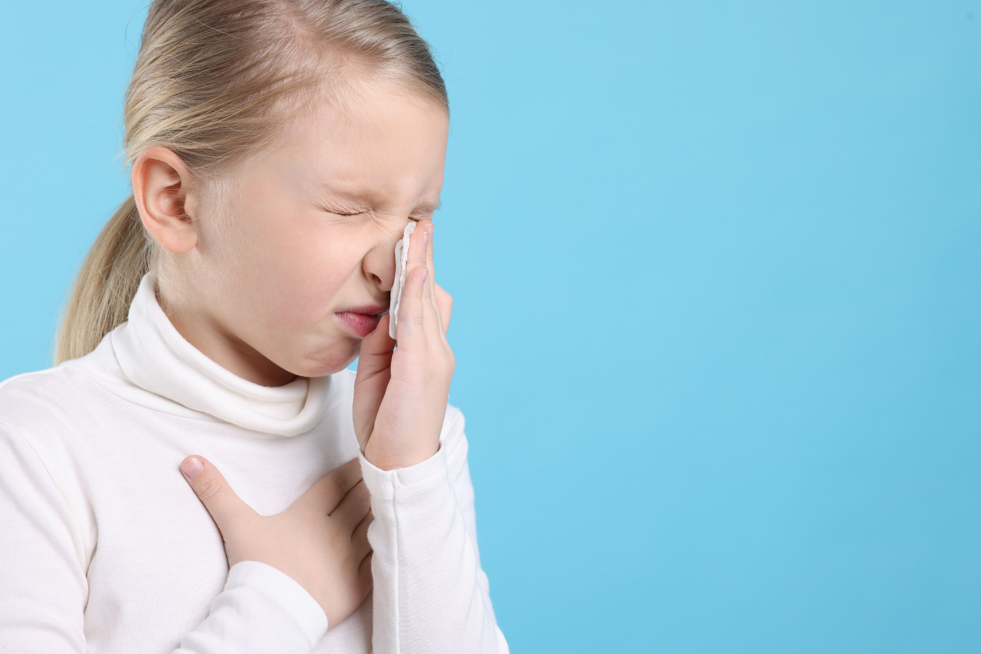 Young child pressing a tissue to their nose with eyes closed against a blue background