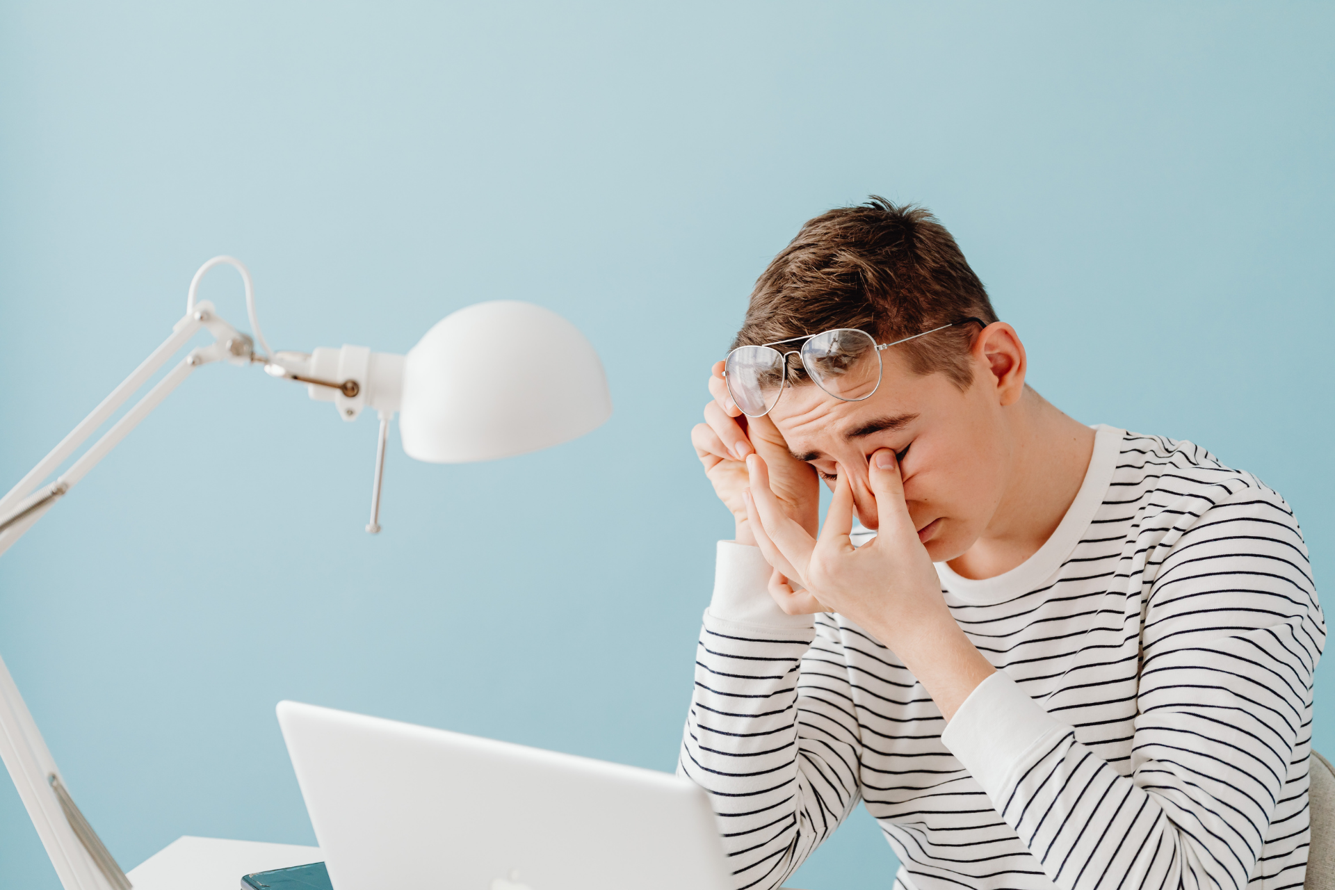 Young person rubbing eyes while sitting at a desk with a laptop