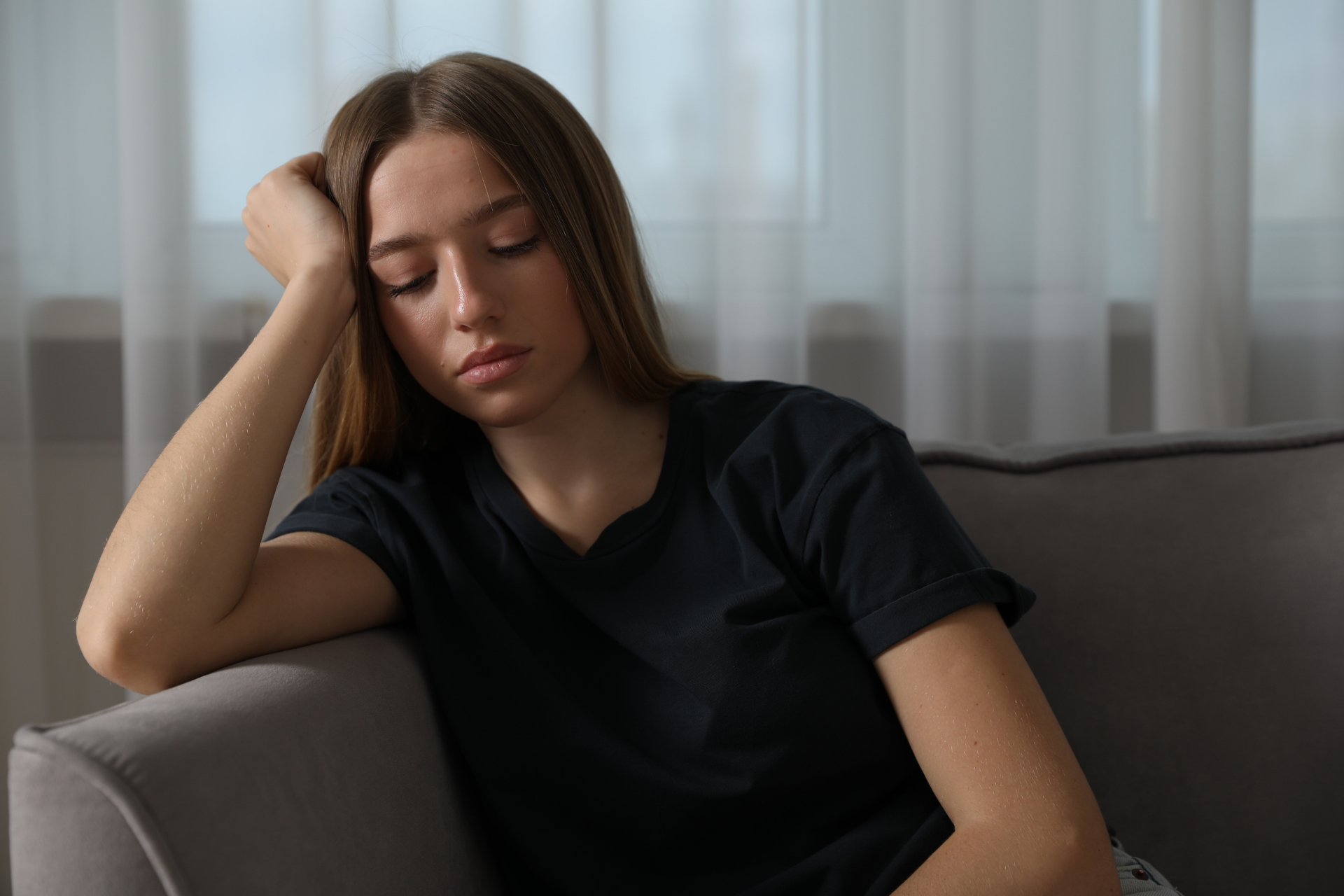 Young woman sitting on a couch with her head resting on her hand, looking tired